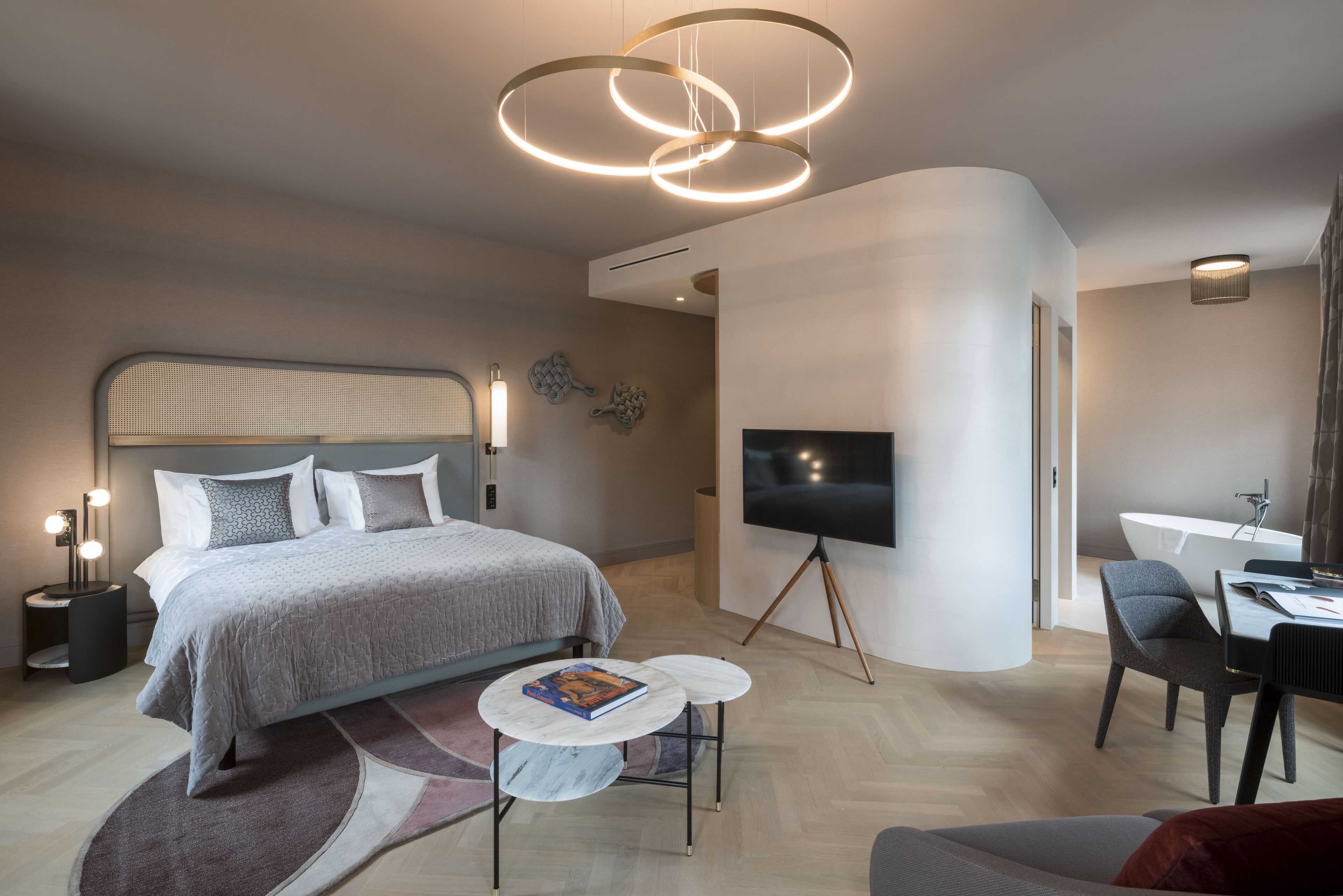 A modern hotel room with a large bed, a flat-screen TV, a desk, and a seating area.