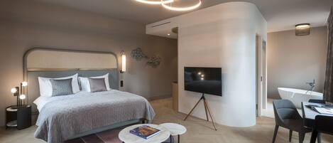 A modern hotel room with a large bed, a flat-screen TV, a desk, and a seating area.