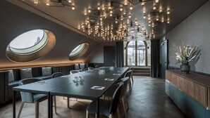 A modern conference room with a long table, comfortable seating, and a unique ceiling design with multiple light fixtures. - Hotel Märthof Basel (Basel)