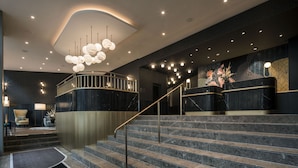 A modern lobby with a marble staircase, a reception desk, and a seating area with a chair and table. - Hotel Märthof Basel (Basel)
