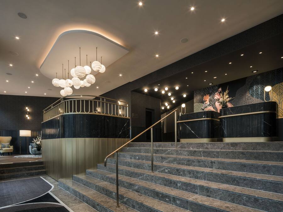 A modern lobby with a marble staircase, a reception desk, and a seating area with a chair and table.