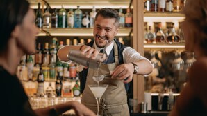A bartender preparing a drink behind a bar with shelves of bottles and glasses. - Hotel Märthof Basel (Basel)