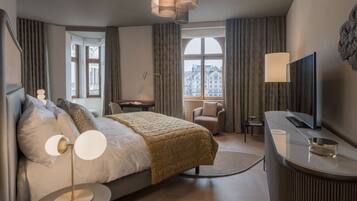 Una habitación de hotel moderna con una cama grande, un escritorio, una silla, un televisor y vistas a la ciudad a través de amplios ventanales.