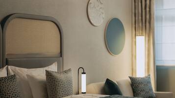 A neatly arranged hotel room with a bed, pillows, a bedside lamp, a wall-mounted mirror, and a window with curtains.