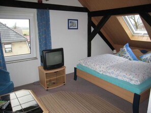 A bedroom with a bed, a television on a wooden stand, a window, and a skylight. - Triple room - Wolter guest room (Lutherstadt Wittenberg)