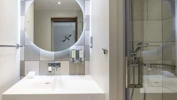 Un baño moderno con un espejo grande, un lavabo blanco y una zona de ducha con mampara de vidrio.