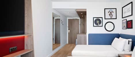 Una habitación de hotel moderna con un televisor de pantalla plana grande, un sofá azul, una cama blanca y una pared decorativa de madera.