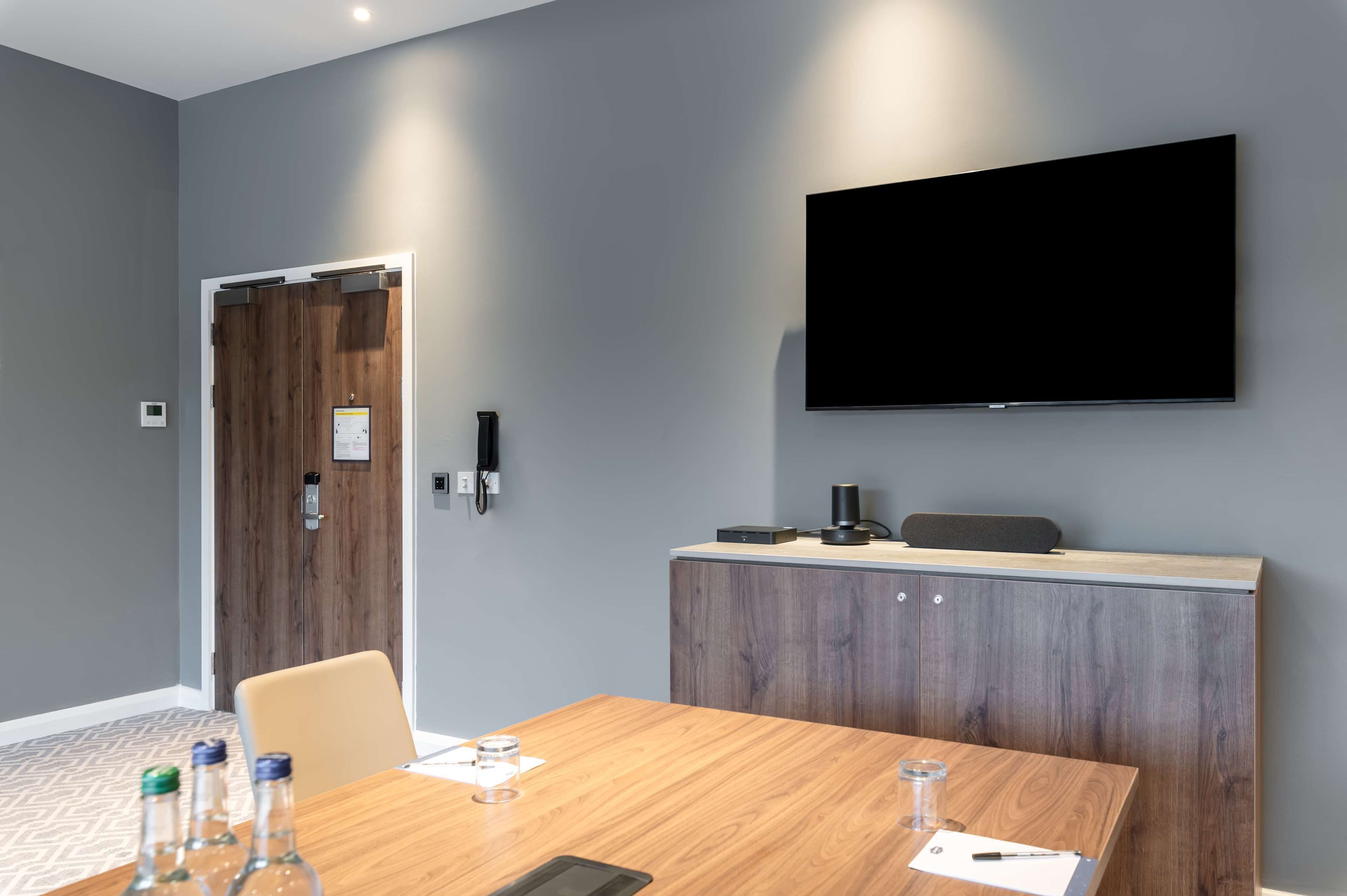 Un salón de conferencias con una mesa de madera, sillas, un televisor de pantalla plana y un mueble de madera.