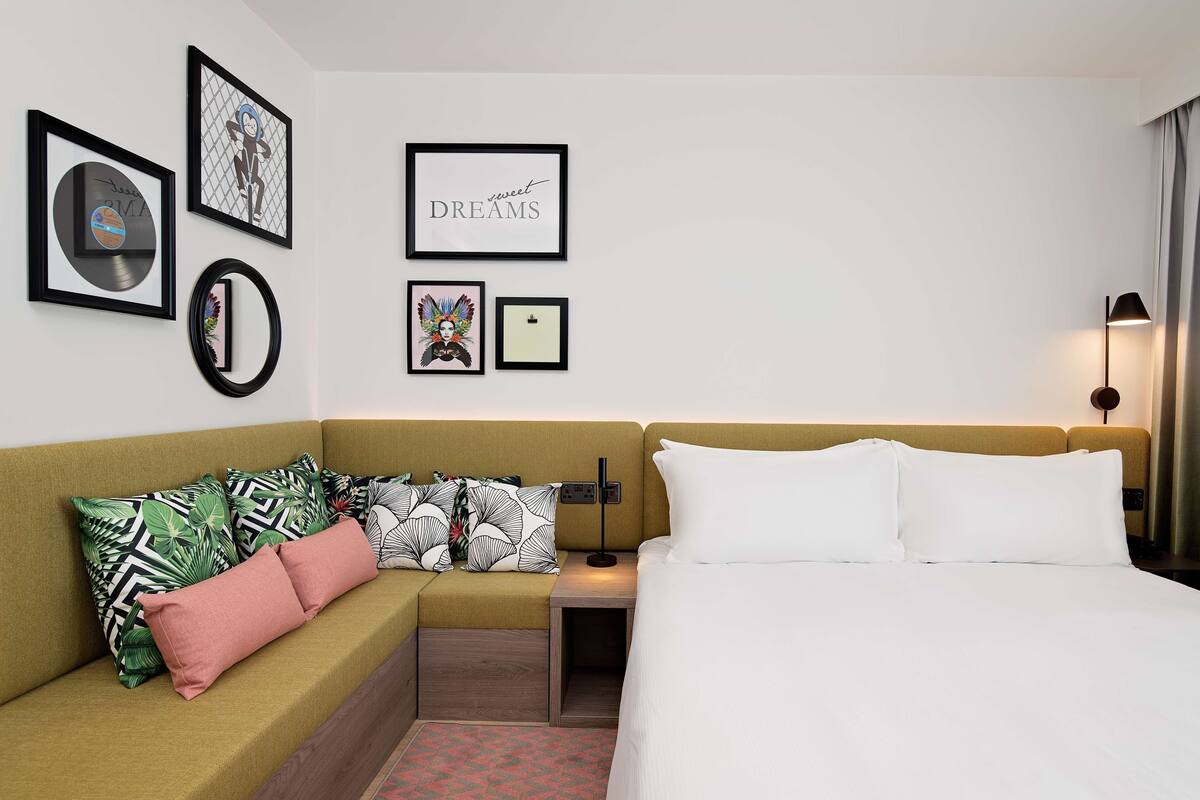 A hotel room with a bed, a sofa, a nightstand, and wall art.
