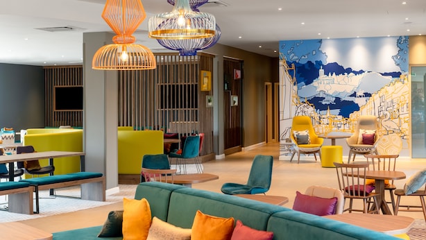 A modern hotel lobby with vibrant seating areas, including sofas and chairs, and a large mural on the wall. - Hampton by Hilton High Wycombe (High Wycombe)