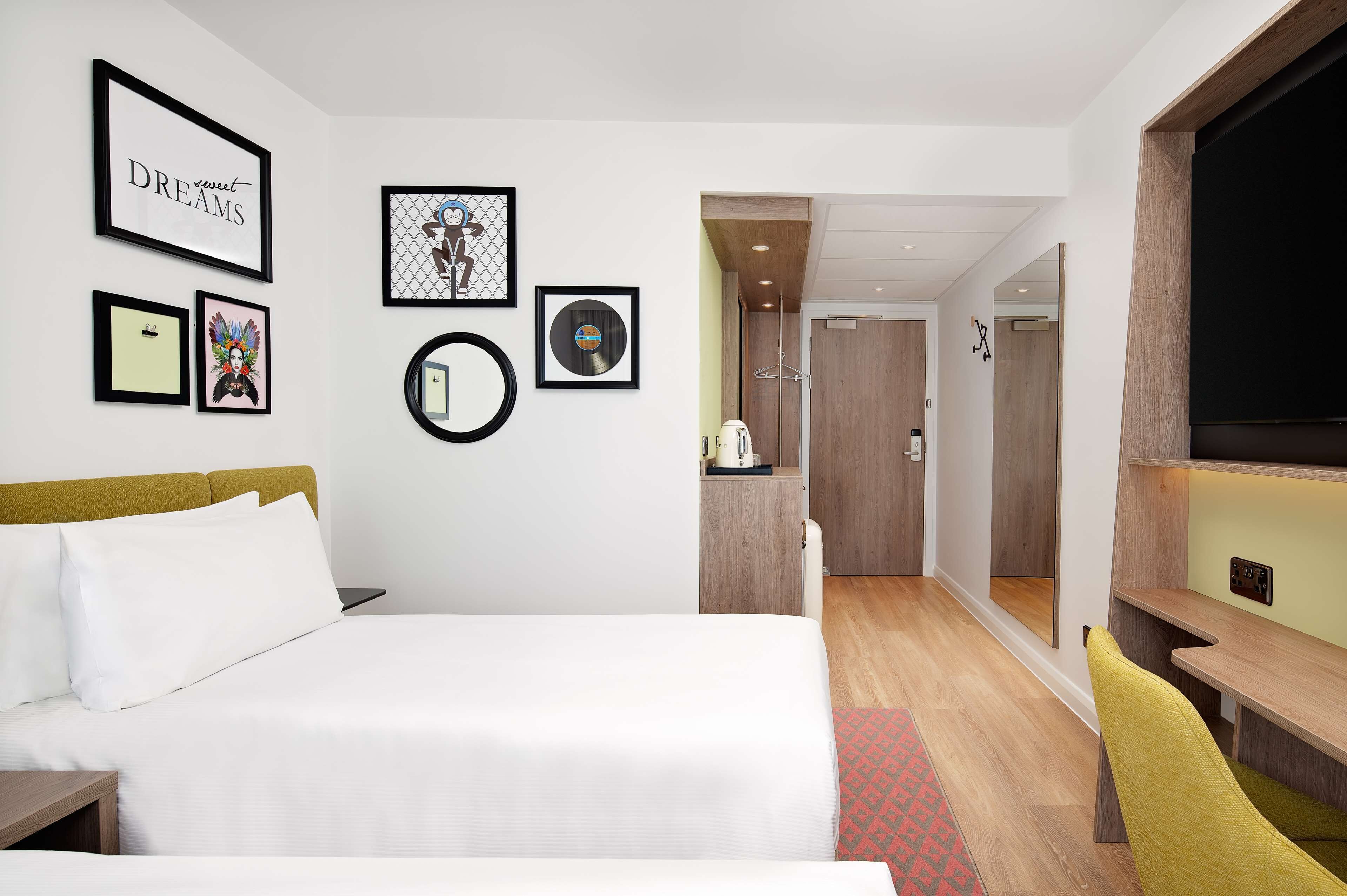 Ein Hotelzimmer mit Bett, Schreibtisch, Spiegel und gerahmten Bildern an der Wand.