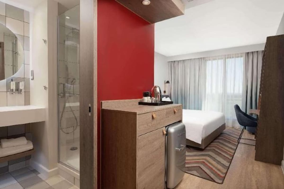 A hotel room with a shower, a bed, a desk, and a chair.
