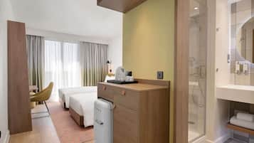 A hotel room with a bed, a desk, a minibar, a shower area, and a view of the outdoors.
