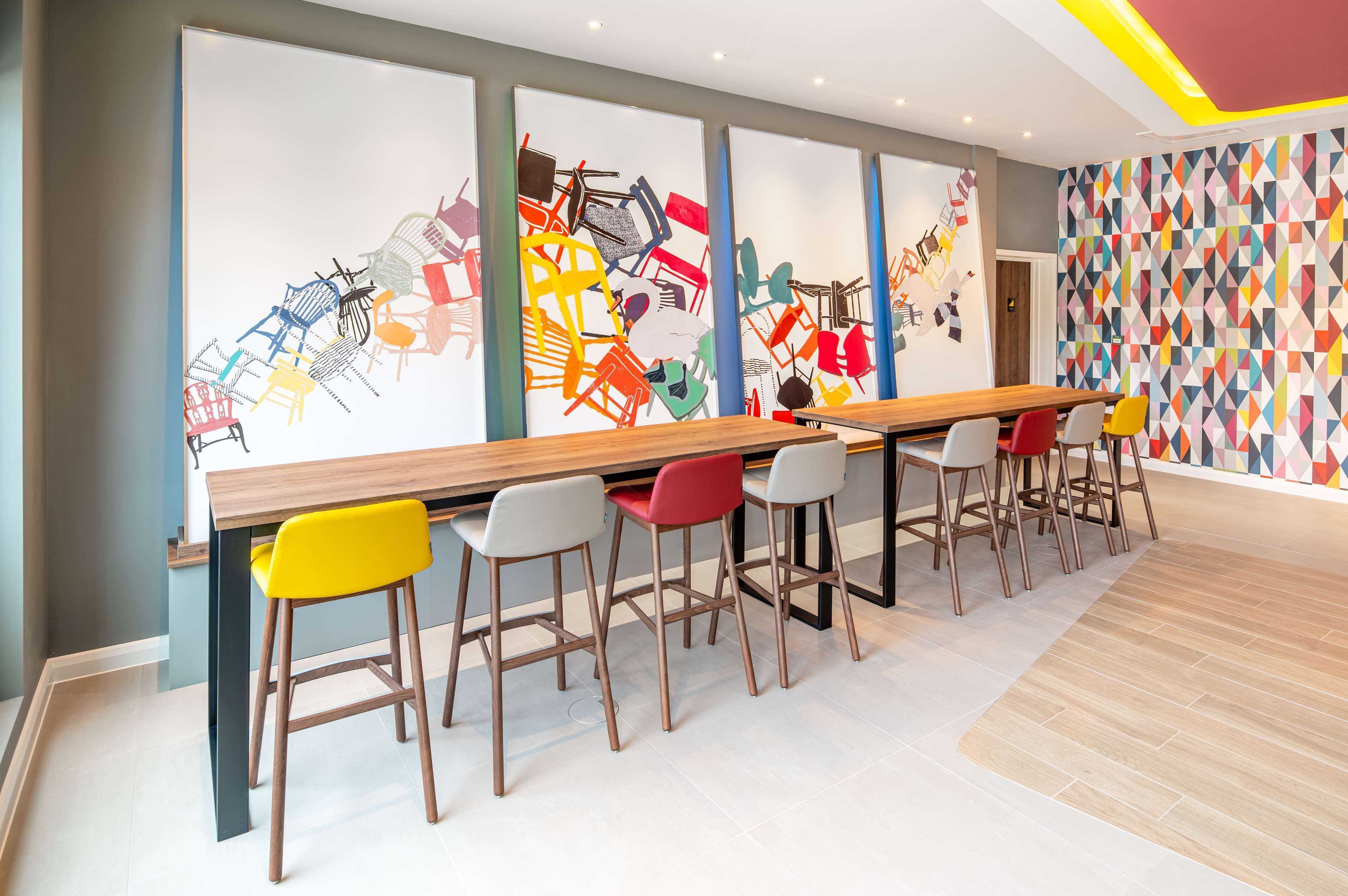 A modern bar area with a long wooden counter and colorful chairs.