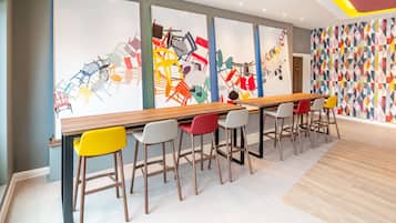 A modern bar area with a long wooden counter and colorful chairs.