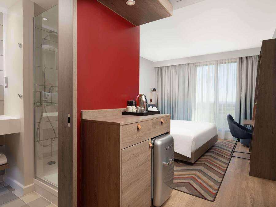 Une chambre d’hôtel avec une douche, un lit, un bureau et une fenêtre avec des rideaux.