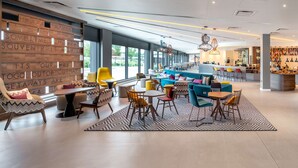 A modern hotel lobby with a bar area, seating arrangements, and a large window providing natural light. - Hampton by Hilton High Wycombe (High Wycombe)