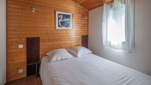 Quarto com teto de madeira, cama com roupa de cama branca, quadro na parede e janela com cortinas.