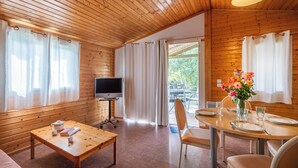 Interior de uma cabana de madeira com televisão, mesa de jantar e sofá.