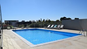 Una piscina rectangular con interior azul, rodeada por un solárium de hormigón. Varias tumbonas y una escalera metálica dan acceso a la piscina.
