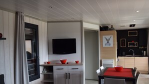 Una cocina moderna con una televisión de pantalla plana, armarios de madera y una zona de comedor con un mantel individual rojo.