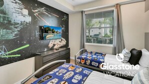 Une chambre d’hôtel avec une fresque murale sur le thème de Star Wars, une télévision, deux lits avec une literie sur le thème de Star Wars et une fenêtre avec des stores.