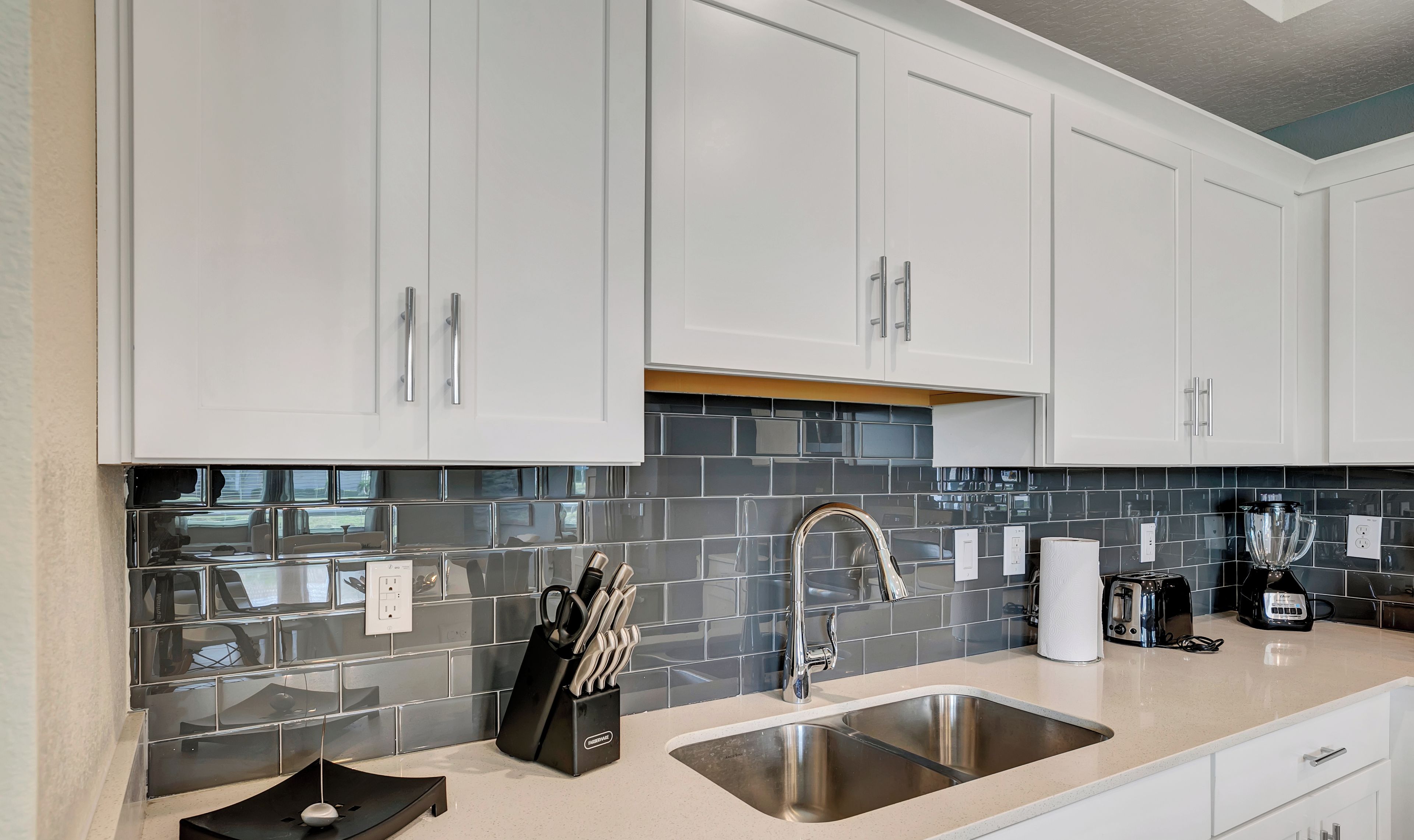 A modern kitchen with white cabinets, a stainless steel sink, and a black knife block.