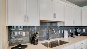 Une cuisine moderne avec des meubles blancs, un évier en acier inoxydable et un bloc à couteaux noir.