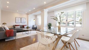 A spacious living room with a glass dining table, white chairs, a grey sofa, and a red throw blanket. - Elkano | The Rentals Collection (San Sebastián/Donostia)