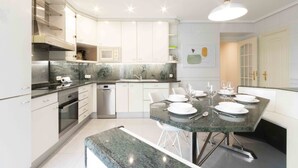 A modern kitchen with white cabinets, a granite countertop, and a dining area with a table set for four. - Elkano | The Rentals Collection (San Sebastián/Donostia)