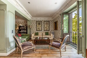 Een ruime woonkamer met een bank, twee fauteuils, een salontafel en een boekenkast.