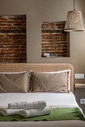 Quarto com parede de tijolos, cabeceira de fibra natural e luminária pendente.