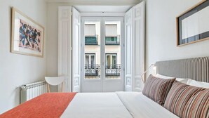 Hotellihuone, jossa on sänky, yöpöytä, lamppu, ikkuna, josta on näkymä parvekkeelle, ja seinällä oleva kehystetty kuva.