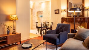 A living room with a sofa, armchair, coffee table, and a lamp. There is a dining area with a table and chairs in the background.