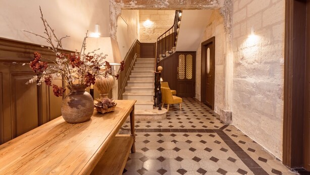 A hallway with a wooden bench, a vase of dried flowers, a staircase, and a patterned floor.