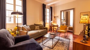A living room with a sofa, armchair, and a coffee table. There is a dining area with a chair and a lamp.