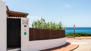 A coastal building with a black gate, a white wall, and a wooden fence with plants. - Mon Palau - House with sea view in Biniancolla (Biniancolla)