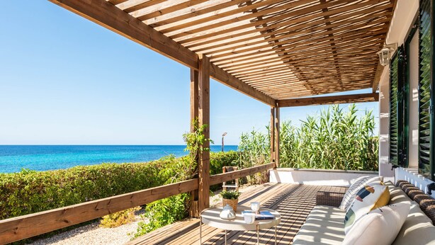 A wooden deck with a view of the ocean, a wicker sofa with cushions, and a small table with a plant and a book. - Mon Palau - House with sea view in Biniancolla (Biniancolla)