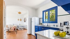 A modern kitchen with blue cabinets, a white refrigerator, and a window with a view of greenery. - Mercè - House with sea view in Biniancolla (Biniancolla)