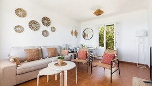 A living room with a sofa, coffee table, wicker chairs, a dining table, and decorative wall art. - Merc è - House with sea view in Biniancolla (Biniancolla)