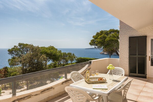 A balcony with a table set for two, overlooking a scenic view of the sea and trees.