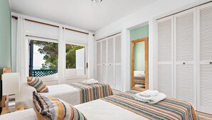 Une chambre d’hôtel avec deux lits, une grande fenêtre et un placard avec des portes à persiennes.