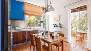 Eine moderne Küche mit Holzschränken, einem Esstisch gedeckt mit Tellern und Tassen sowie einem Fenster mit Jalousien.