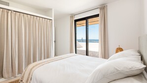 Un dormitorio con cama, cortinas, una ventana con vistas y una mesita de noche con lámpara.