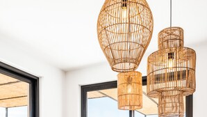 Comedor con mesa y sillas de madera, un cuenco de fruta y lámparas colgantes de mimbre.