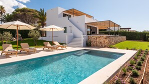 Una casa moderna con piscina, mobiliario exterior y un muro de piedra.