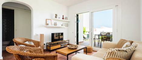 A modern living room with wicker furniture, a flat-screen TV, and a balcony with a view.