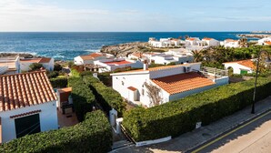 A coastal residential area with white buildings, red-tiled roofs, and a clear view of the sea.