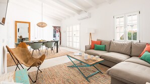 A modern living room with a sofa, a coffee table, and a chair. There is a dining area in the background with a table and chairs.