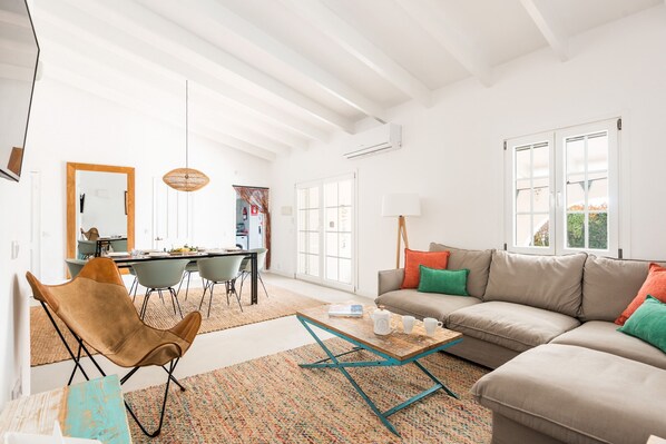 A modern living room with a sofa, a coffee table, and a chair. There is a dining area in the background with a table and chairs.
